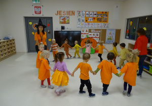 dzieci ubrane na pomarańczowo tańczą w kole
